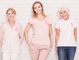 A row of smiling women wearing pink ribbons on their shirts