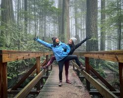 Two women in winter hiking clothes pose on a wooden footbridge.