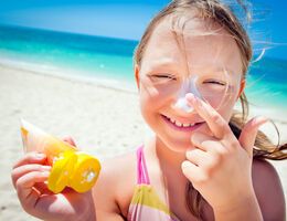 Girl applying sunscreen to her nose at the beach.
