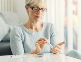 A woman checks her blood sugar at a coffee table.