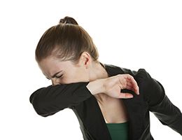 A woman sneezes into her elbow.