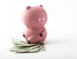 A piggy bank sitting on a pile of $20 bills.