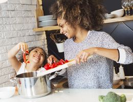 A woman and a young girl laugh as they add peppers to a pot.