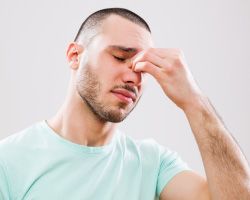 A man with a sinus headache pinches his nose