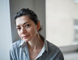 A middle-aged woman is looking at the camera with her head slightly tilted.