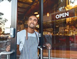 A young man is opening the door to a restaurant. The door has a sign on it that says "open."