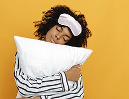 A woman wearing a sleep mask and hugging a pillow.