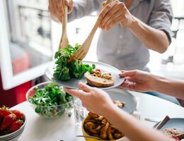 A person uses salad forks to scoop salad onto a plate beside half of a bagel.