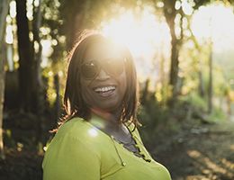 A smiling woman wearing sunglasses outdoors.