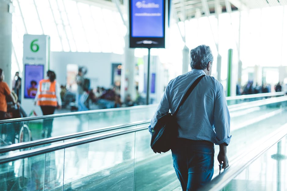 A man with a backpack walks through an airport terminal near a moving walkway.