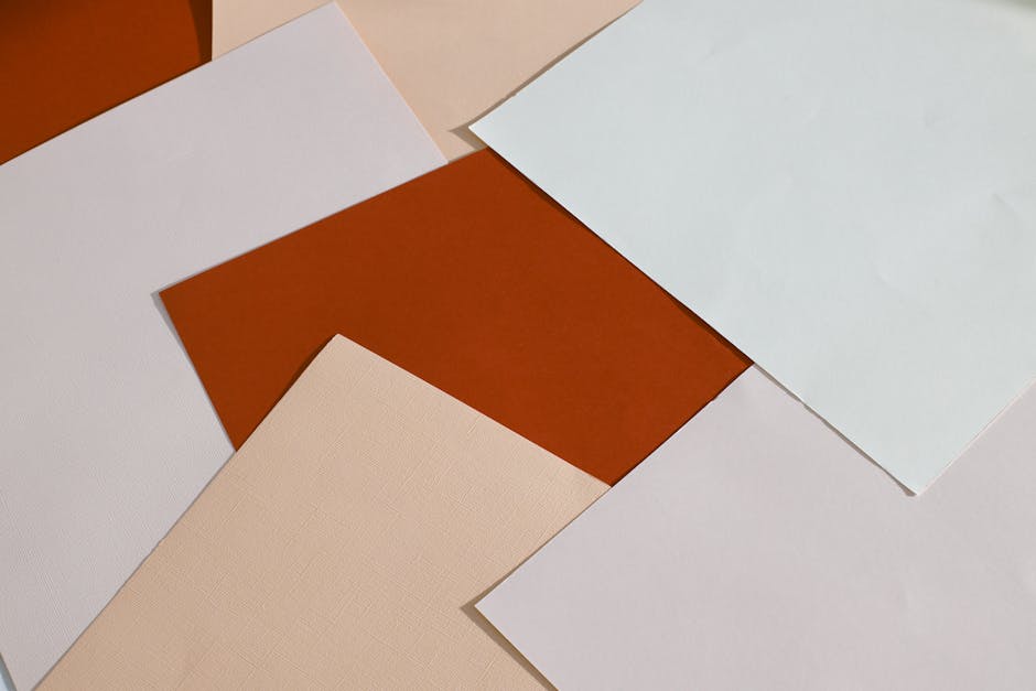 Several sheets of blank paper in various shades of white, beige, and brown are overlapping on a flat surface.