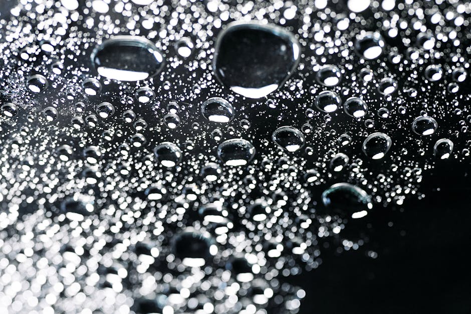 Close-up image of water droplets on a dark, reflective surface, creating a sparkling, abstract pattern.