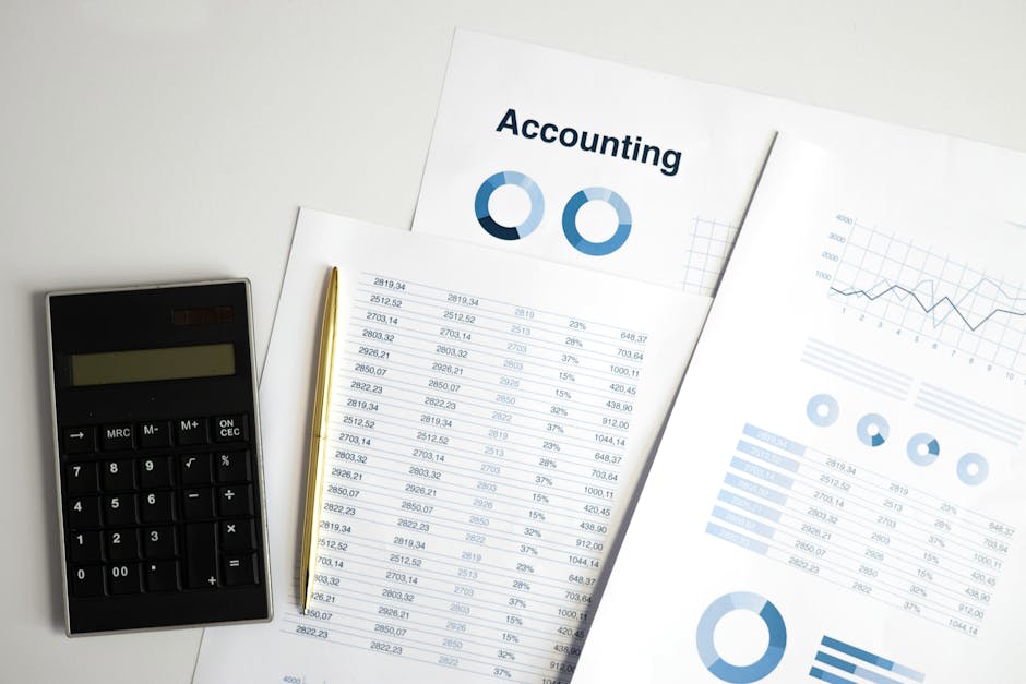 Image of an accounting setup with a calculator, financial documents, and graphs. The documents include numeric data and circular and line graphs, focusing on the subject of accounting.