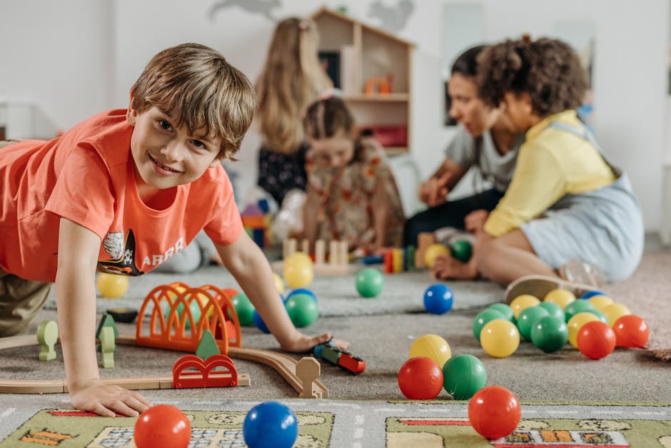 Children playing with toys and colorful plastic balls on the floor in a playroom or daycare.