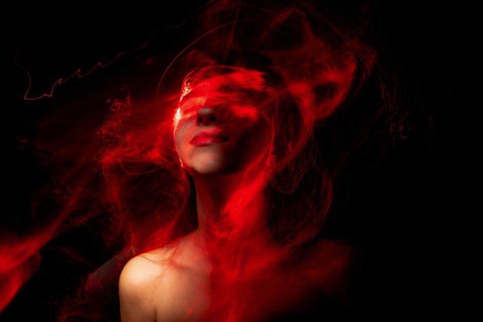 An abstract image of a woman's face mostly obscured by swirling red light trails against a black background.
