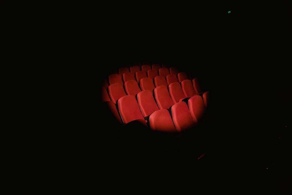 A spotlight illuminates rows of empty red theater seats in a darkened room.
