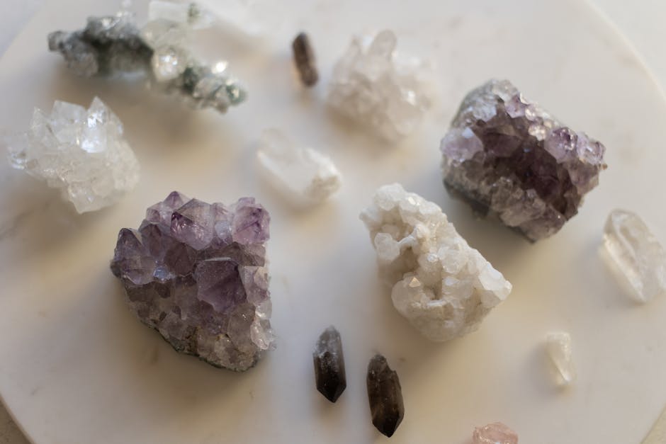 An arrangement of various rough crystals and minerals, including purple amethyst and clear quartz, displayed on a light surface.