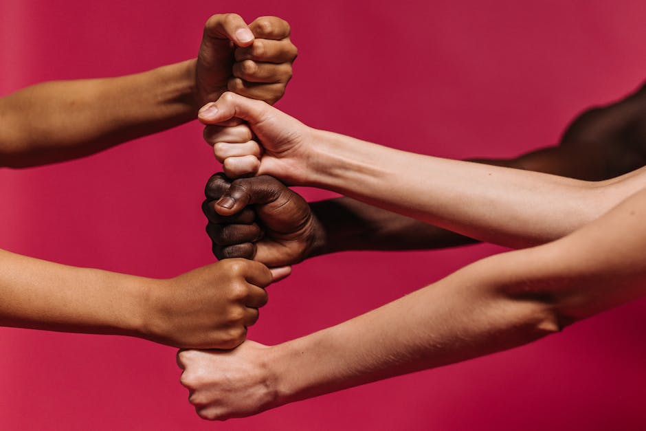 A group of diverse hands coming together in a collaborative gesture against a vibrant pink background, symbolizing unity and teamwork.