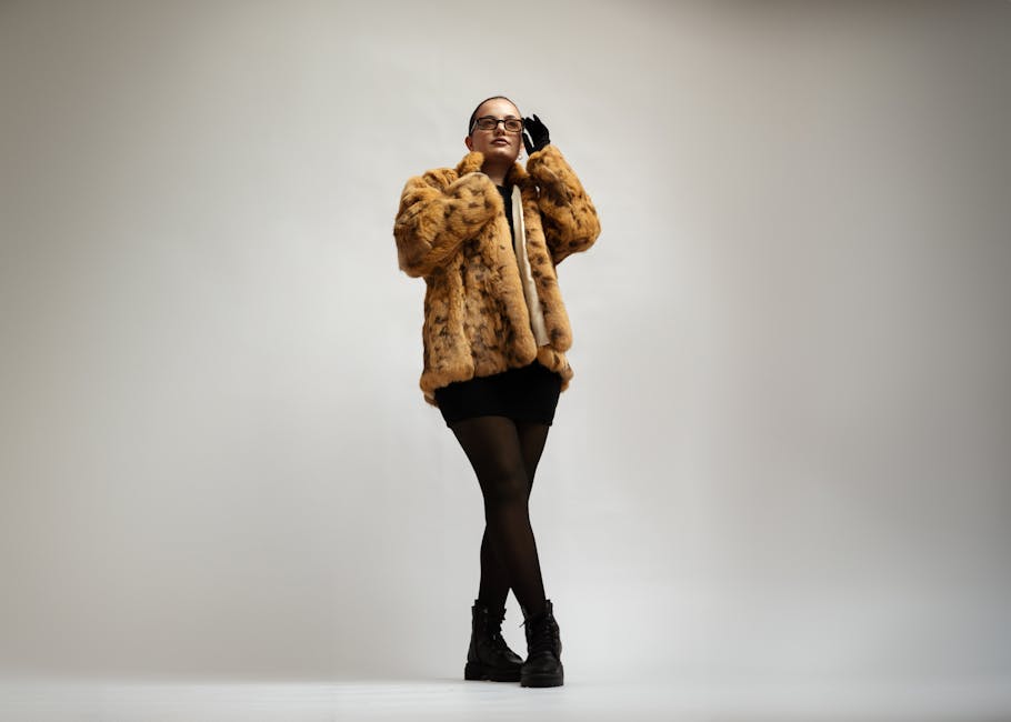 A person wearing a faux fur coat, black glasses, and gloves poses confidently against a minimalist backdrop.