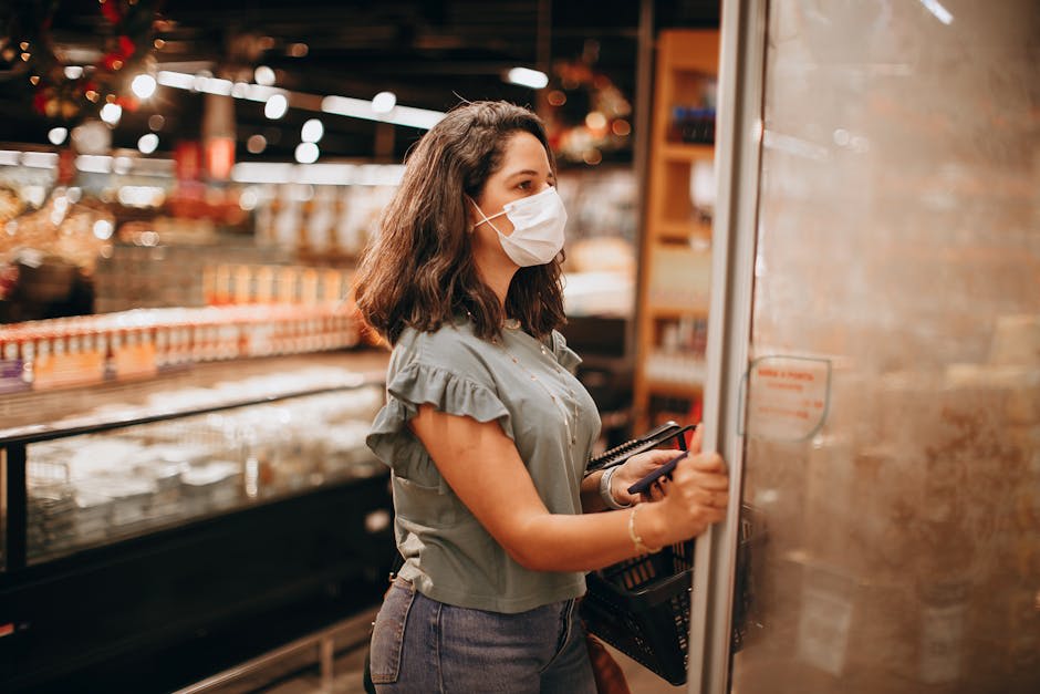 A woman wearing a face mask opens a refrigerator door while shopping in a grocery store.