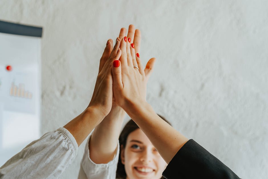 A group of people giving a high-five together in an office setting. The image captures multiple hands joining in a symbolic gesture of teamwork and success, with a blurred chart in the background suggesting a business context.