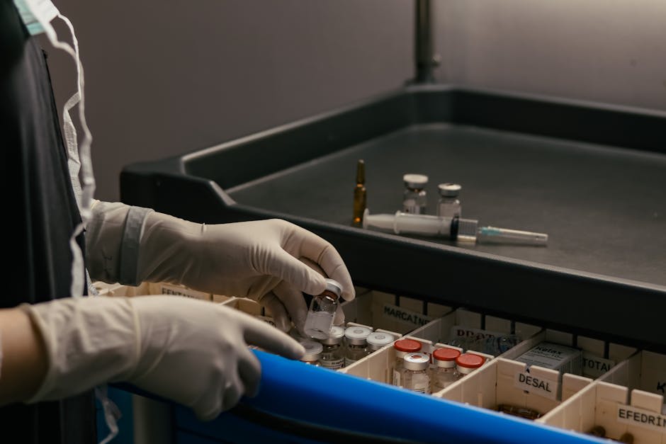 A gloved healthcare worker organizes vials and medical supplies in a compartmentalized tray.