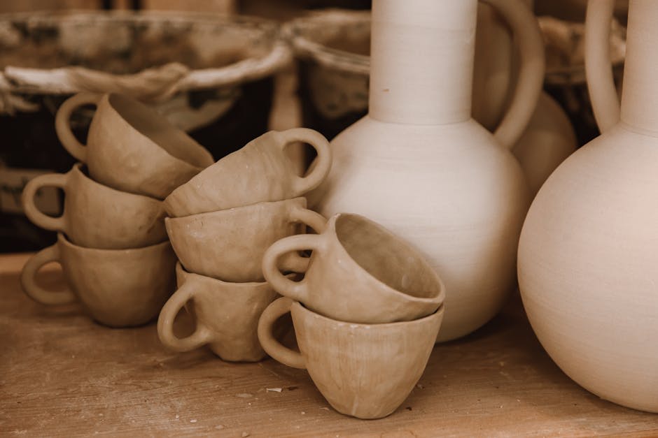 The image shows a stack of unfinished ceramic cups alongside large pottery vessels on a wooden surface.