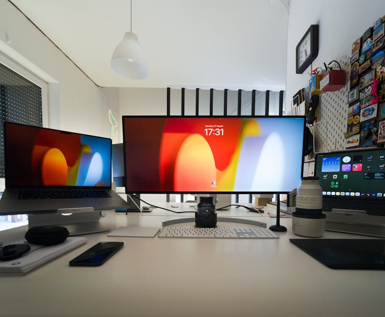 A modern workspace setup with an ultra-wide monitor in the center, two additional screens on either side, a camera placed in front of the main screen, and various tech gadgets and accessories on the desk.
