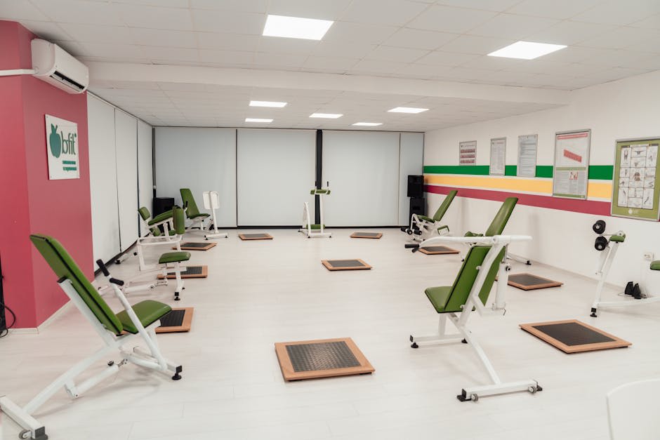 A well-lit indoor gym with rows of green exercise chairs and wooden platforms arranged in a spacious layout.