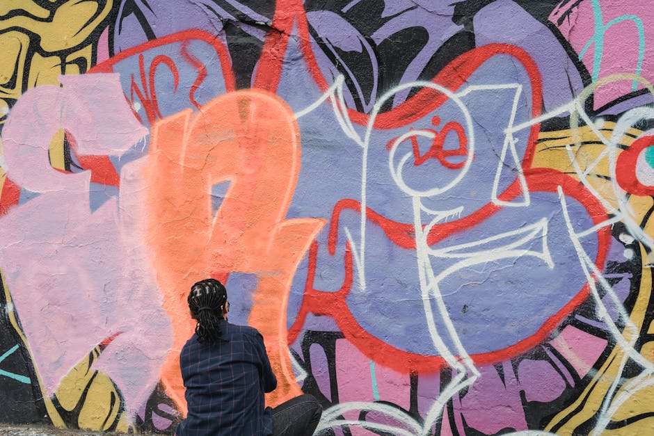 A person with braided hair is spray painting colorful graffiti on a wall.