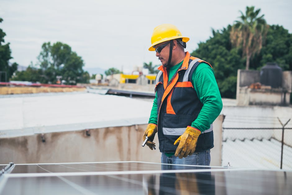 A construction worker wearing a hard hat and safety vest is inspecting solar panels outdoors.