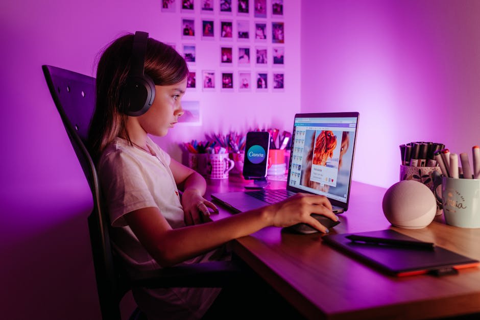 A young person wearing headphones is sitting at a desk using a laptop with a design editing application open, surrounded by pens, mugs, and other desk tools, illuminated by vibrant purple lighting.