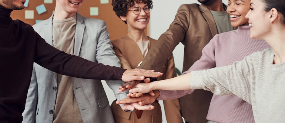 A group of diverse individuals standing in a circle with their hands stacked in the center, symbolizing teamwork and unity in a professional office setting.
