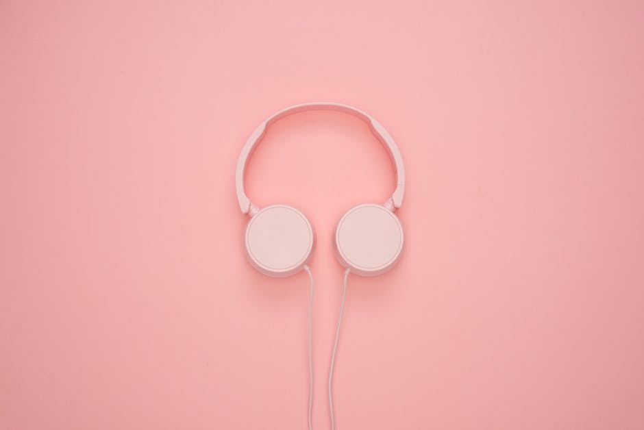 A pair of white wired headphones is placed against a pastel pink background.