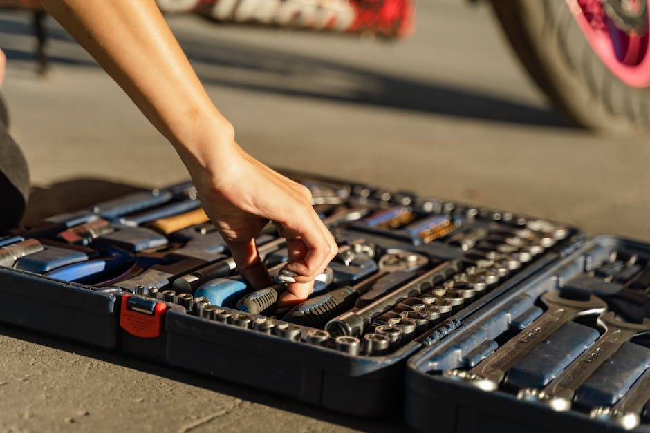 A person is selecting a tool from an organized toolkit laid open on the ground, with a focus on their hand and the tools.
