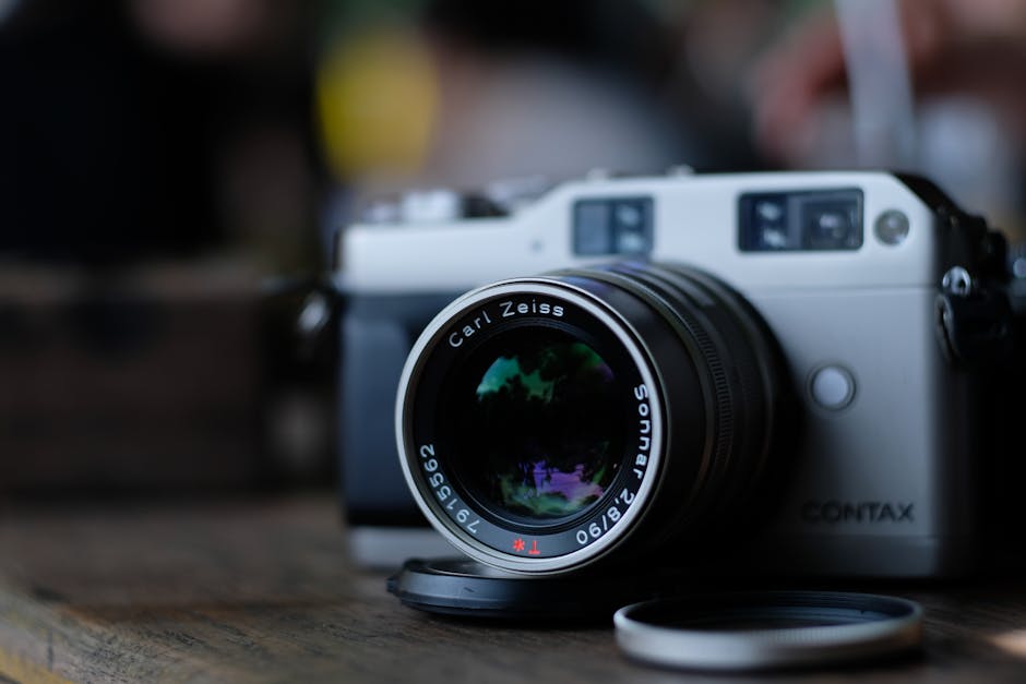 A close-up shot of a silver Contax film camera with a Carl Zeiss Sonnar lens placed on a wooden surface.