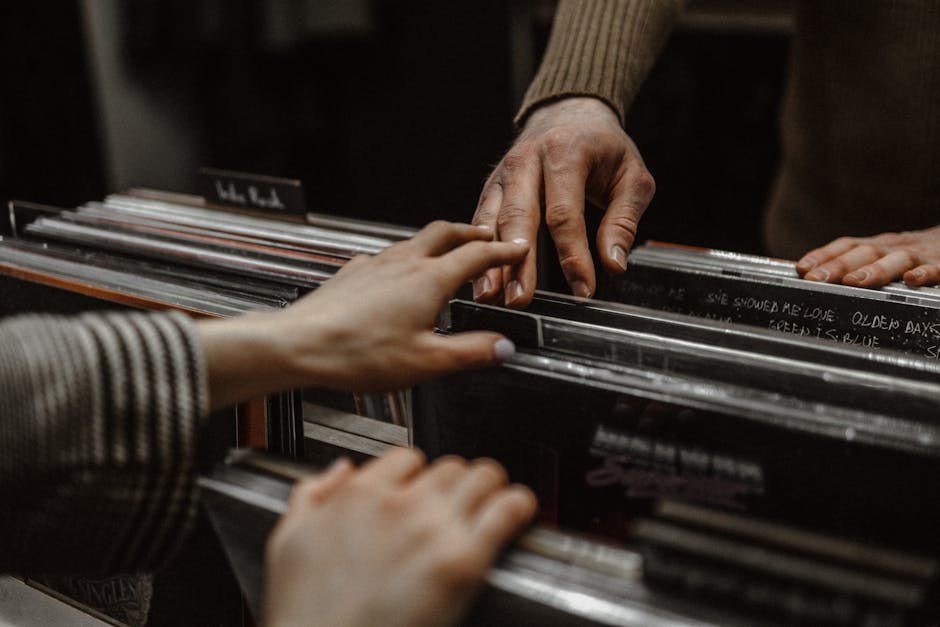 Two people’s hands are reaching towards vinyl records displayed in a store.
