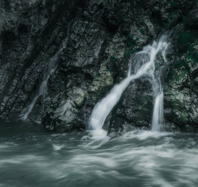 A small, natural waterfall cascades down moss-covered rocks into a swirling pool of water.