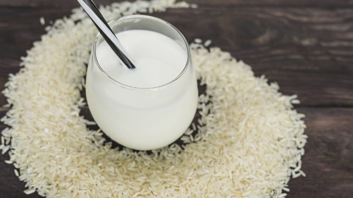A glass of cloudy rice water sits beside a small white bowl of uncooked rice, a simple aid for weight loss.