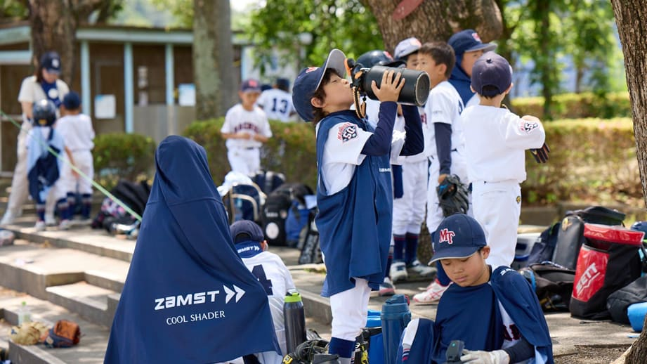 十八軒アトムズの青いユニフォームを着た少年が、笑顔で両手を広げて歓迎。チームでの楽しい野球体験を象徴するイラスト。