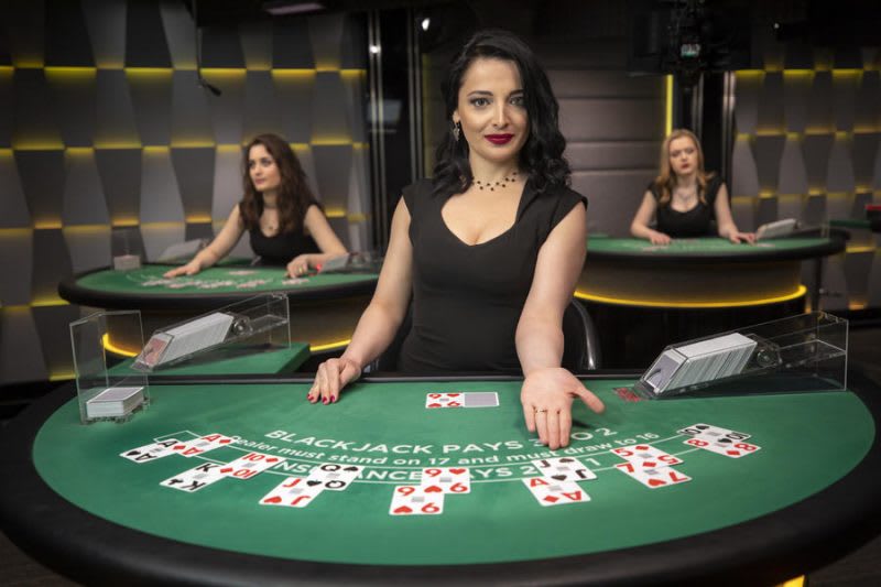 A female dealer at a live casino blackjack table deals cards, showcasing the realism that differs from RNG table games.