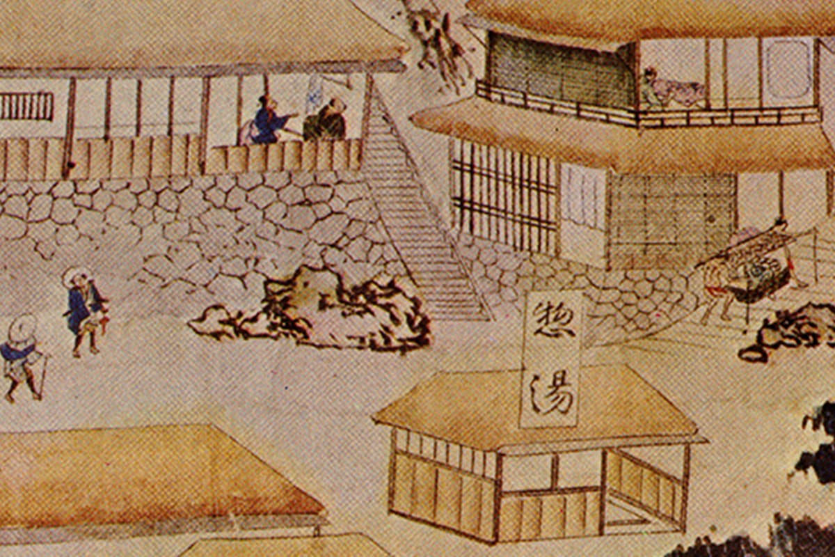 人々が有馬温泉「金の湯」前の足湯でくつろぐ。赤褐色の名湯に足をつけ、風情ある木造建物の下で温泉街の魅力を満喫する様子。