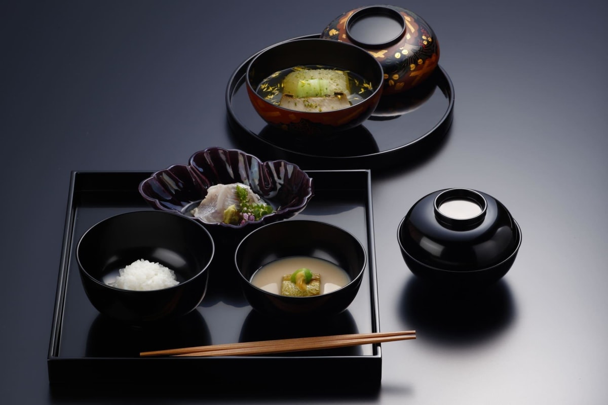 黒いお膳に美しく配膳された懐石料理。焼き魚、ご飯、汁物、小鉢からなる献立が、伝統的な日本の食事様式を示す。