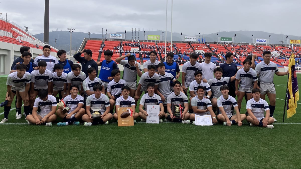 高校ラグビーの熱闘で、強豪校の選手たちが力強いスクラムを組む。黒と黄色のジャージのチームが、青いユニフォームの相手を押し込もうと奮闘している。