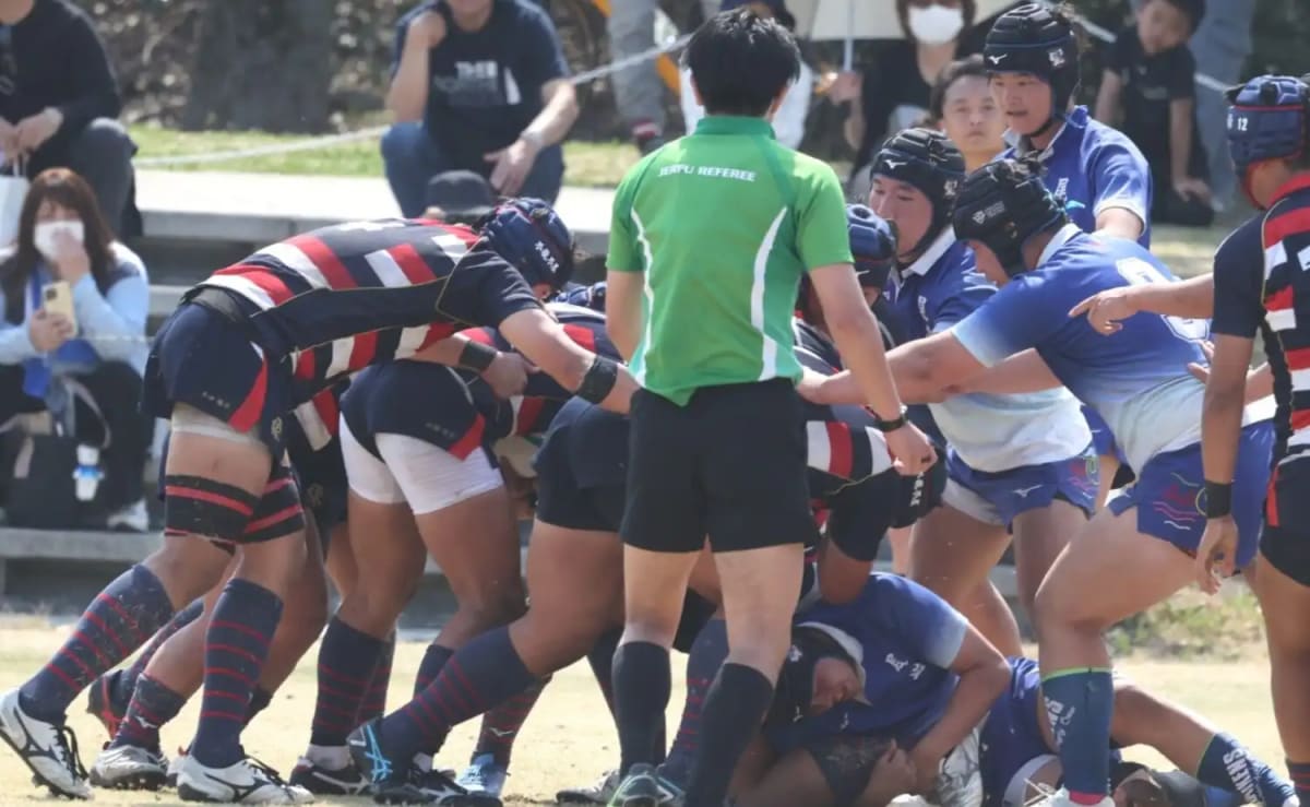 高校ラグビー選手たちが花園で円陣を組む。青いジャージで肩を寄せ、進路決定にも似た試合前の緊張感を共有する。