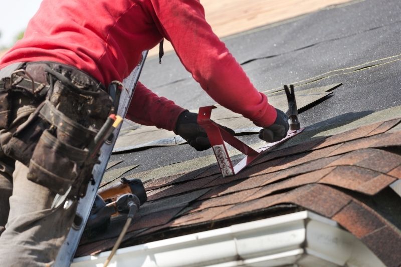 Roofer on residential roof inspecting shingles