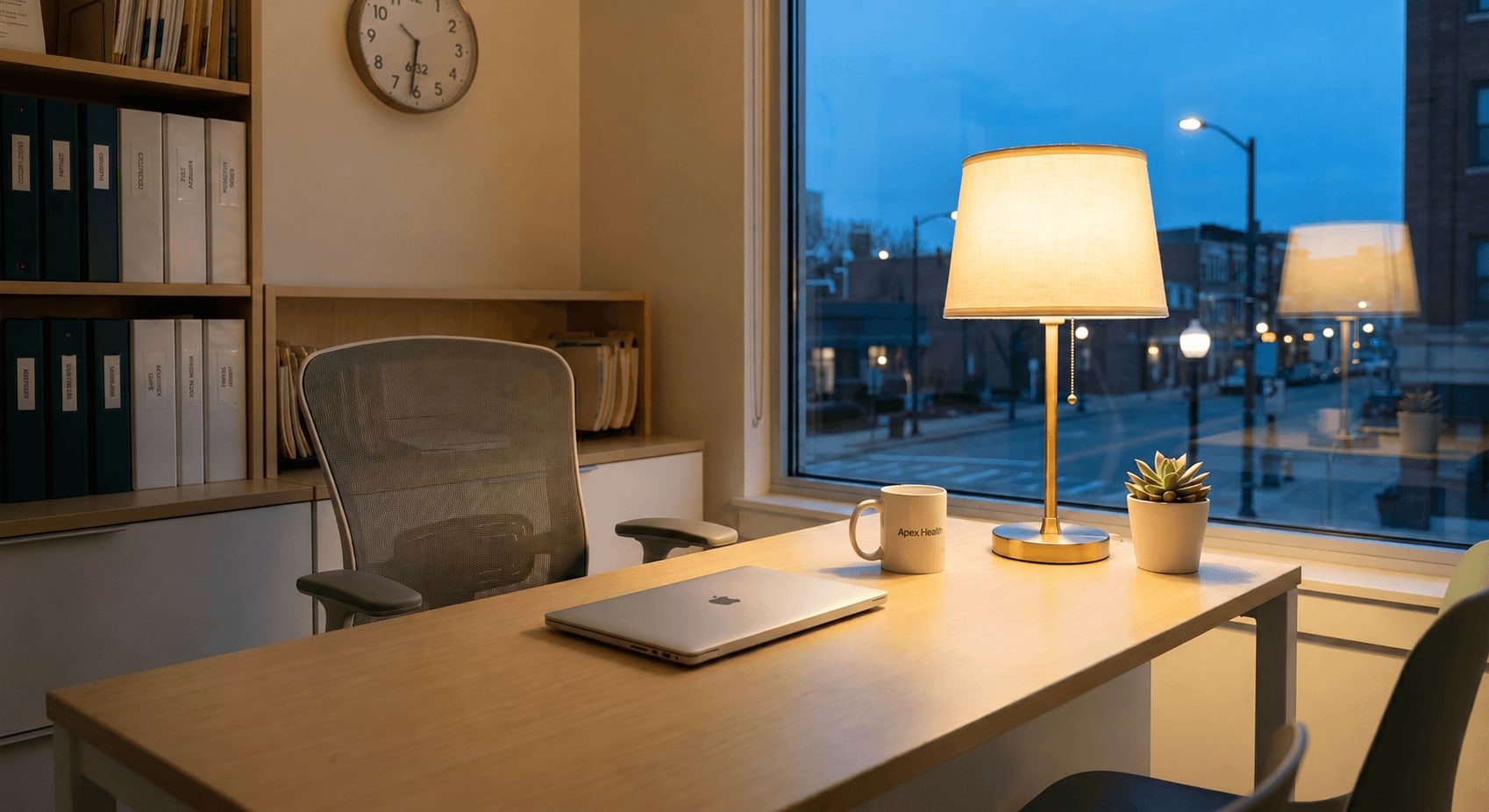 Tidy back-office desk with a laptop and lamp at dusk