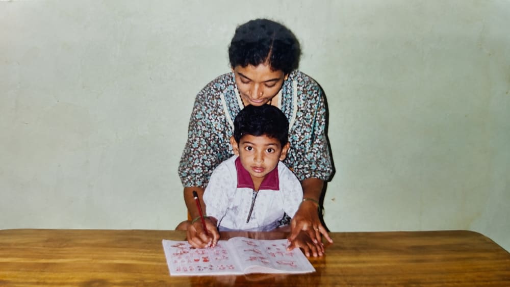 A young mother helping her son with his handwriting at a wooden desk