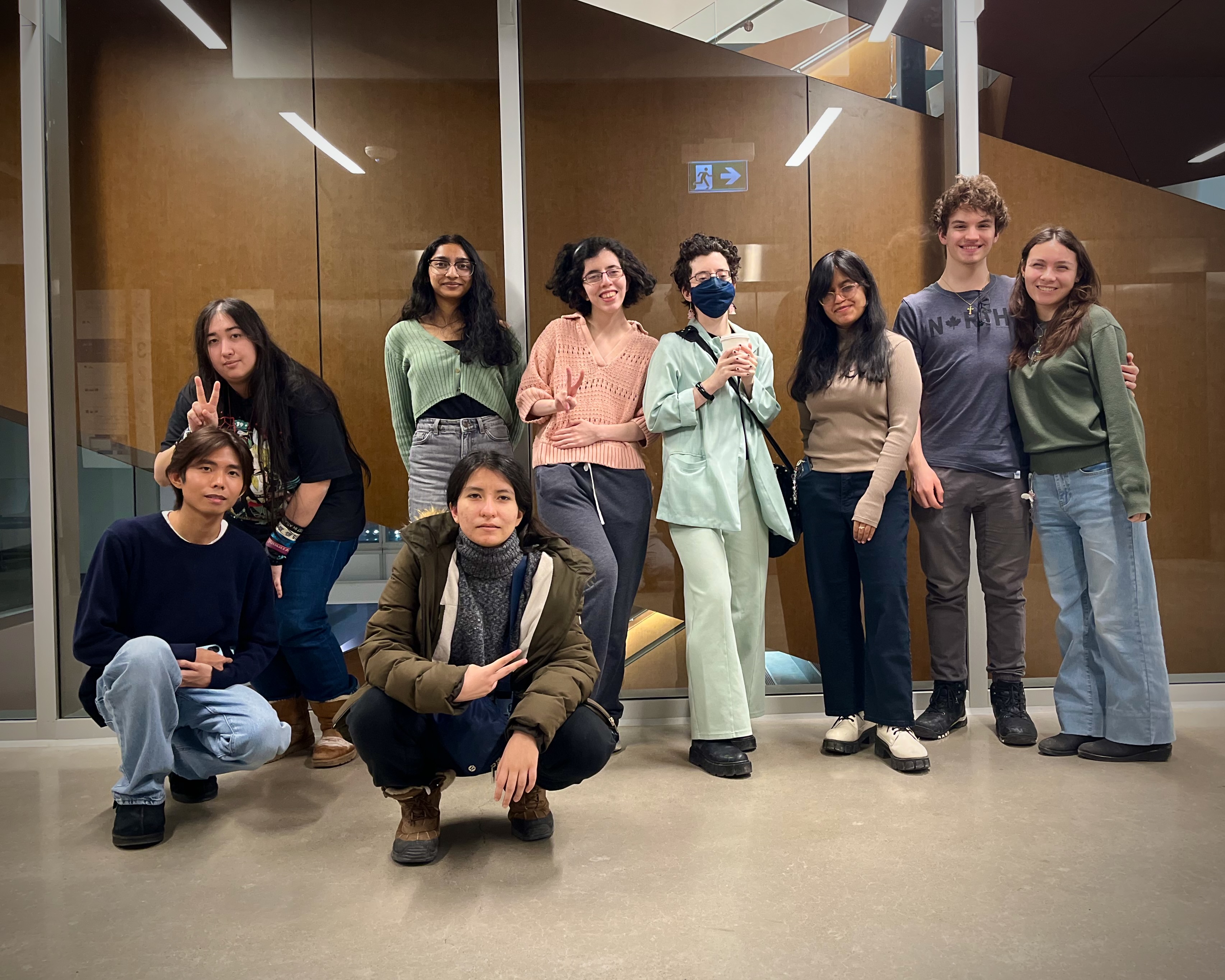 Group of university students pose, in two rows, in the hallway of a university building.