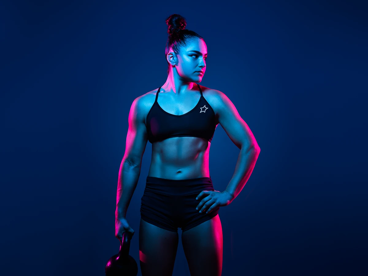 strong woman holding a kettle bell with gel style lighting